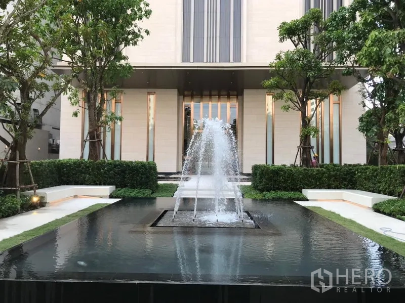 Condominium for rent or sale in Watthana, Bangkok - Elegant condo entrance with central water fountain, trimmed hedges and tall facade