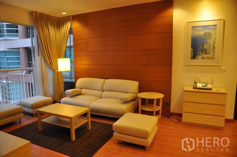 คอนโด ให้เช่าหรือขายในKhlong Toei, Bangkok - มุมนั่งเล่นอบอุ่น โซฟาครีม พร้อมสตูool ผนังไม้ตกแต่ง และหน้าต่างบานใหญ่