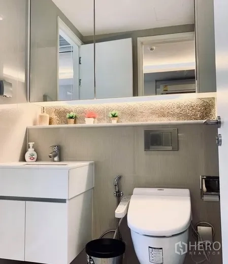 Condominium for rent in Watthana, Bangkok - Modern bathroom with wall-hung vanity, mirrored cabinets, and toilet with bidet spray.