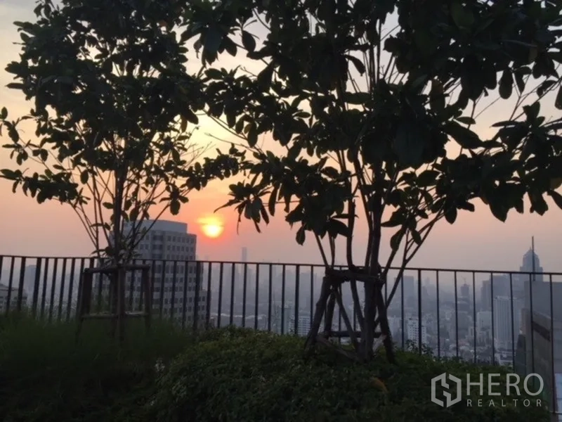 公寓 出租在Watthana, Bangkok - 屋顶花园日落景观，有树木与栏杆俯瞰城市。