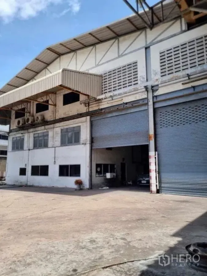 Warehouse for rent in Phra Pradaeng, Samut Prakan - Front facade of the warehouse with office block, two large roller shutter doors and truck-access yard under canopy.