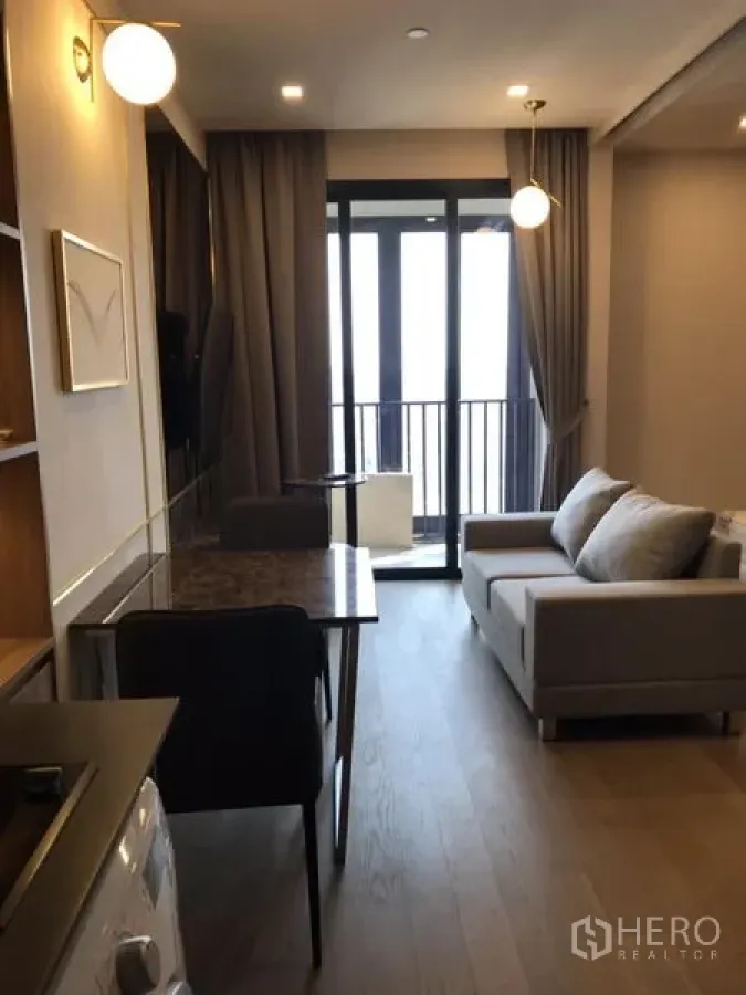 Condominium for rent in Watthana, Bangkok - Modern condo living area with gray sofa, dining table, kitchenette, washing machine and balcony doors in Watthana, Bangkok.