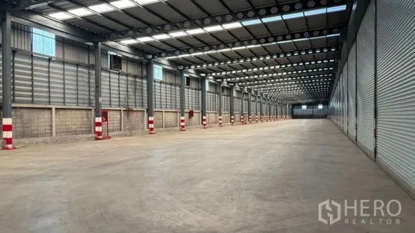 Warehouse for rent in Bang Phli, Samut Prakan - Loading corridor with multiple roller shutter doors, fire safety cabinets, and red‑white column protectors.