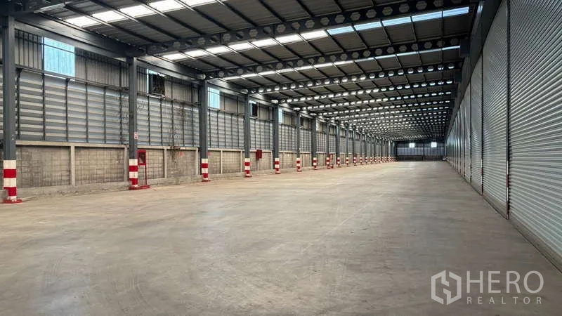 Warehouse for rent in Bang Phli, Samut Prakan - Loading corridor with multiple roller shutter doors, fire safety cabinets, and red‑white column protectors.