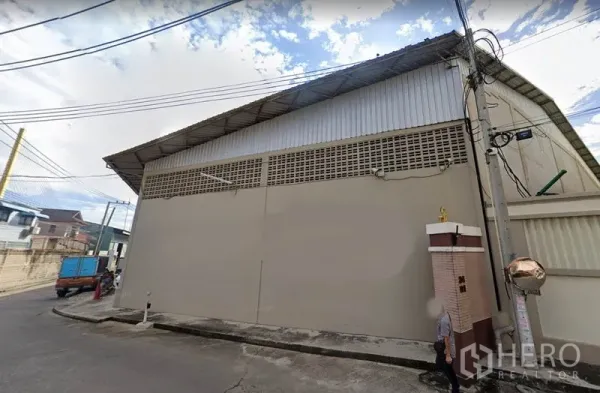 Warehouse for rent in Rat Burana, Bangkok - Street-side exterior of a secure warehouse in Rat Burana, Bangkok with high metal roof, solid concrete wall, and overhead utility lines.