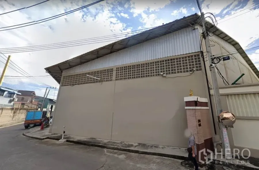 Warehouse for rent in Rat Burana, Bangkok - Street-side exterior of a secure warehouse in Rat Burana, Bangkok with high metal roof, solid concrete wall, and overhead utility lines.