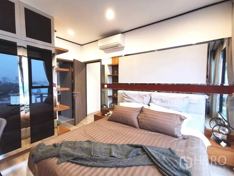 Condominium for rent in Huai Khwang, Bangkok - Bedroom featuring a mirrored wardrobe, built‑in shelving and panoramic window in a Bangkok apartment.