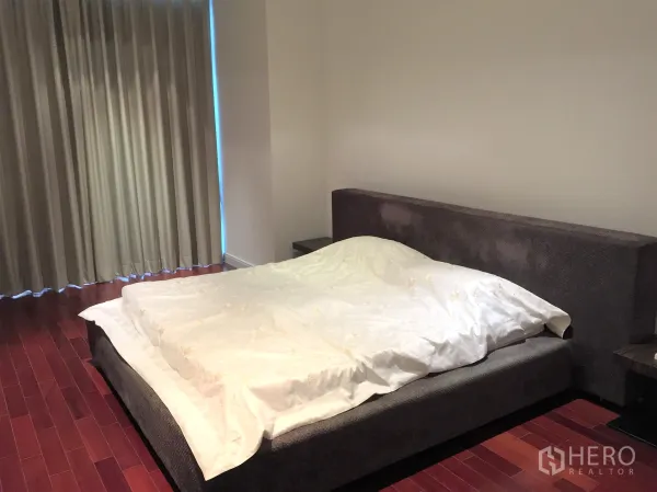 Condominium for rent in Pathum Wan, Bangkok - Primary bedroom with large upholstered bed, rich hardwood floors and blackout curtains.