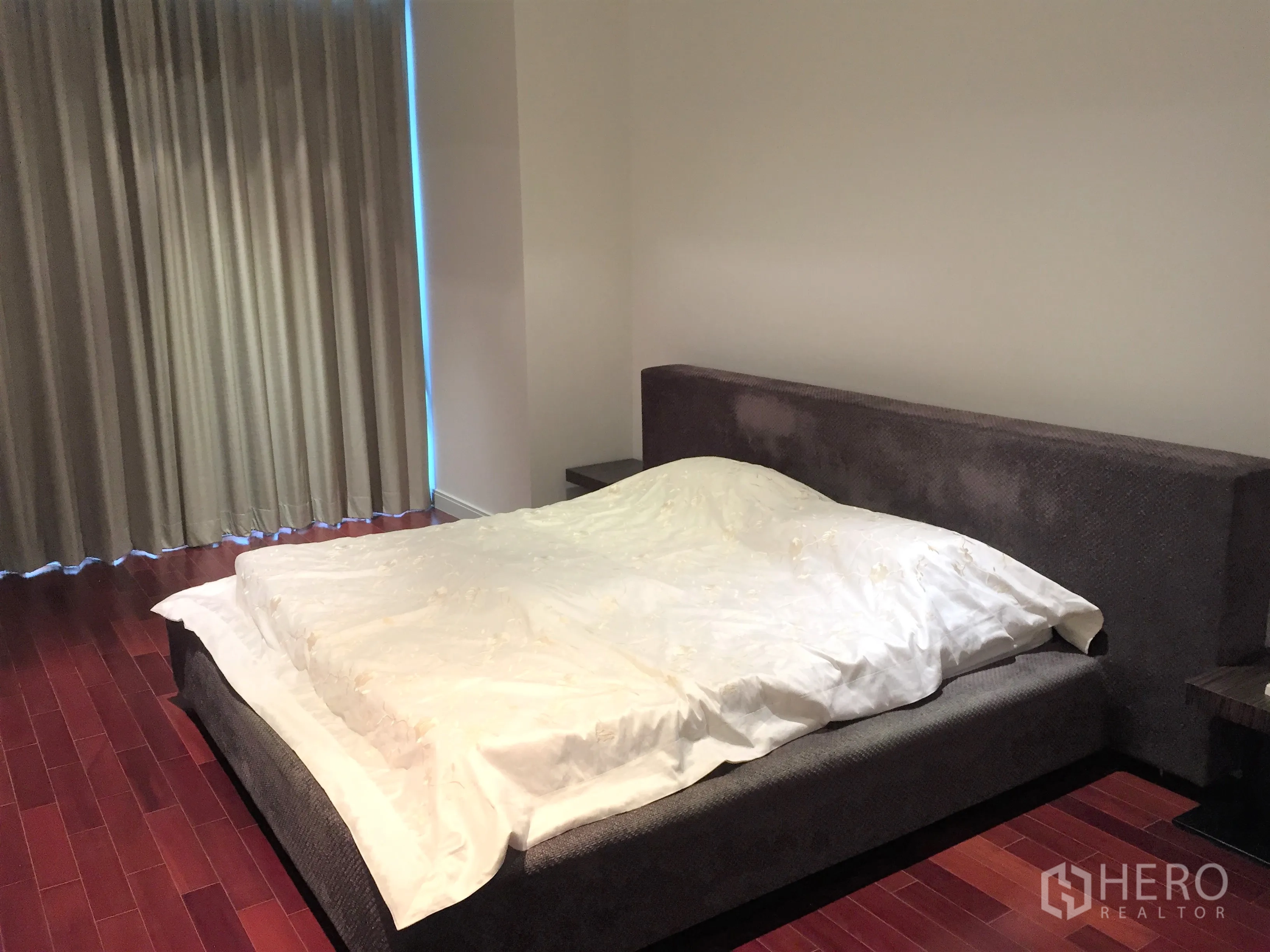 Condominium for rent in Pathum Wan, Bangkok - Primary bedroom with large upholstered bed, rich hardwood floors and blackout curtains.