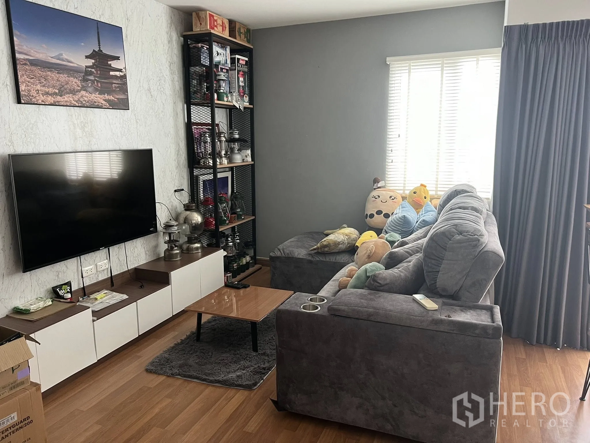 Detached House for rent or sale in Don Mueang, Bangkok - Living zone with wall-mounted TV, shelving and corner sofa.