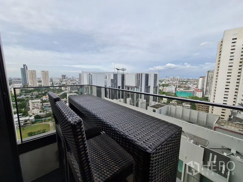 Condominium for rent - Balcony with rattan bar table and chairs, glass railing and wide Bangkok city view.