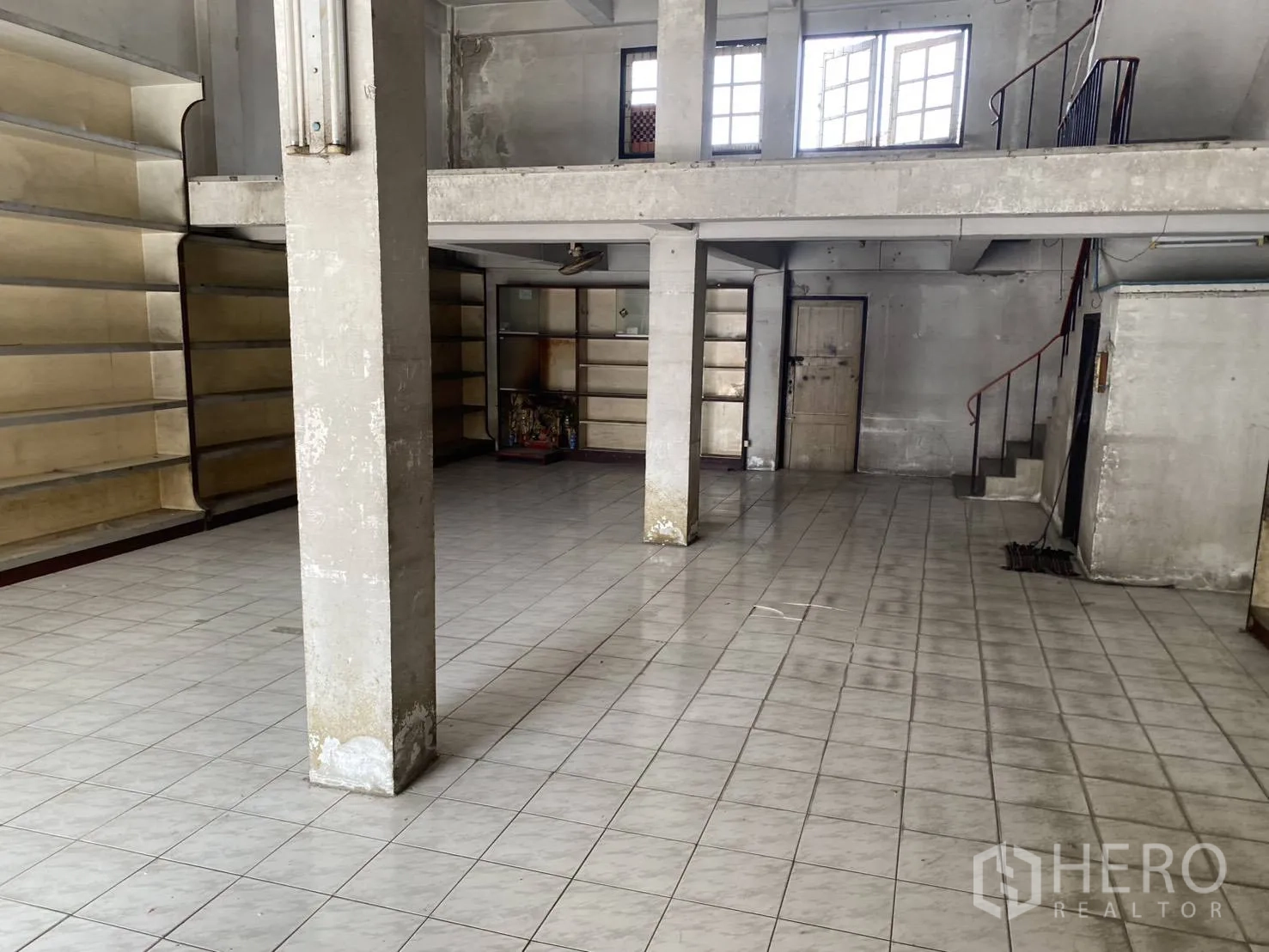 Shophouse for rent in Bang Na, Bangkok - Ground-floor retail space with tiled floor, concrete columns, built-in shelving and internal staircase.
