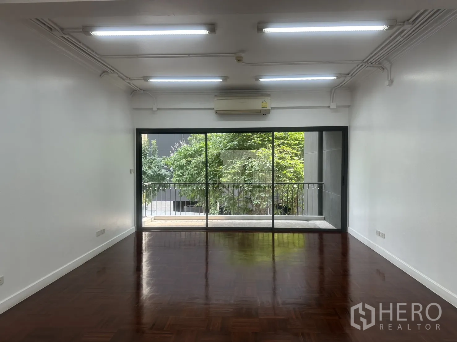 办公室 for rent in Watthana, Bangkok - 开放式办公区，拼花木地板与长条灯，落地滑门通向可见绿景的阳台。