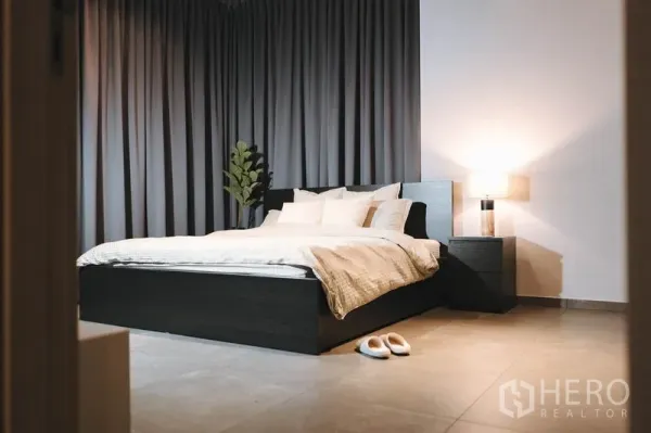 Condominium for rent in Watthana, Bangkok - Cozy master bedroom with dark drapes, bedside lamp, and a queen bed with neutral bedding.