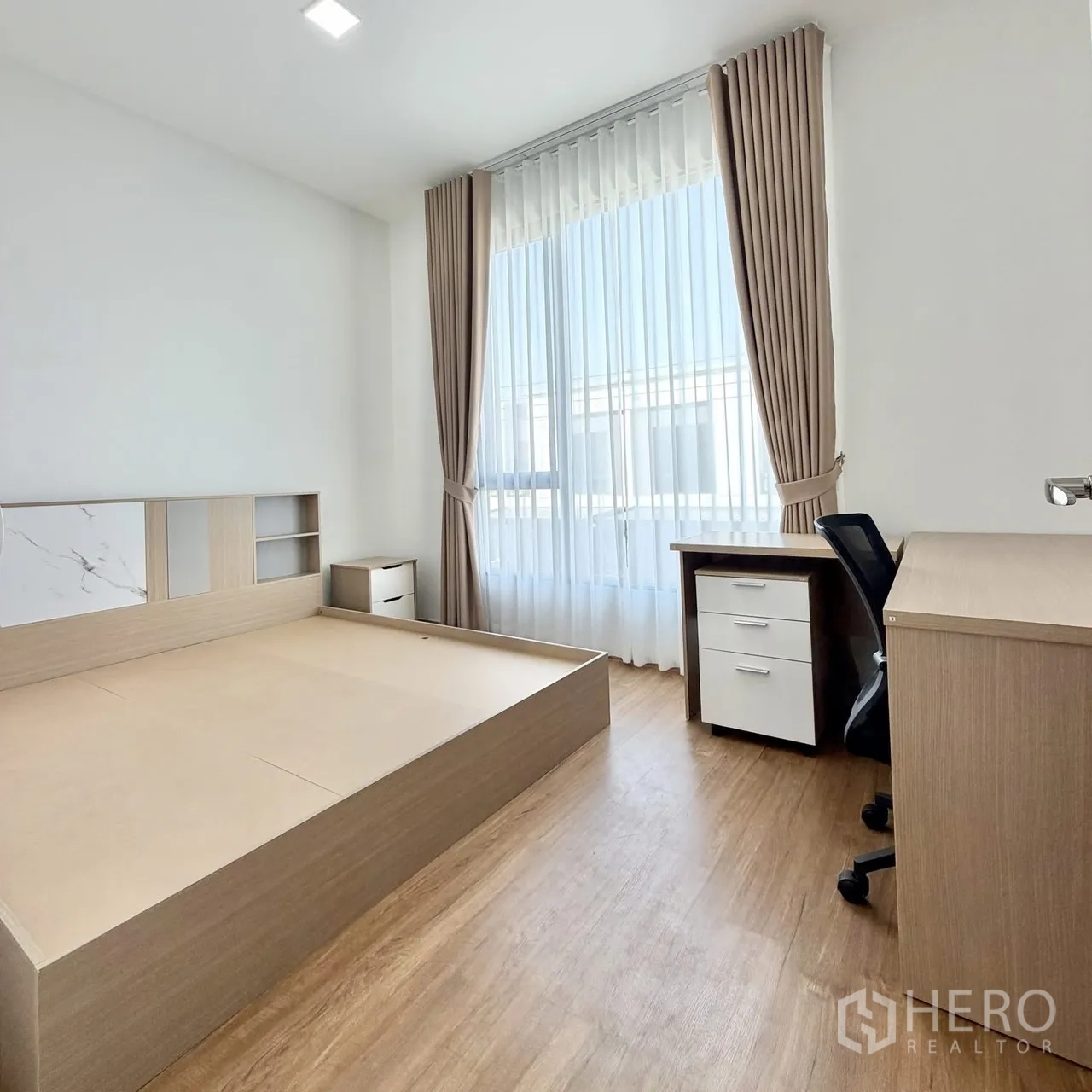 Townhouse for rent in Bang Phli, Samut Prakan - Sunlit master bedroom with platform bed, study desk, and large window with sheer curtains.