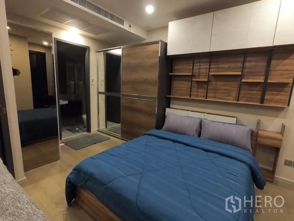 Condominium for rent in Watthana, Bangkok - Bedroom corner featuring built-in shelving, overhead cabinets, and a wood-finished sliding wardrobe with mirror.