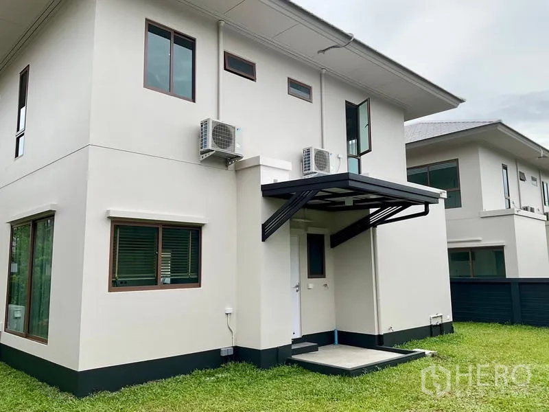 Detached House for rent in Bang Kapi, Bangkok - Rear exterior of the house with green lawn, service door canopy and outdoor AC units.
