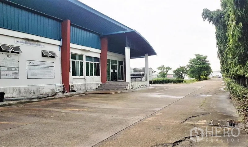 โรงงาน ขายในLam Luk Ka, Pathum Thani - มุมข้างอาคารโรงงาน ทางขึ้นสำนักงาน ทางวิ่งคอนกรีตกว้าง และแนวสวนหย่อม
