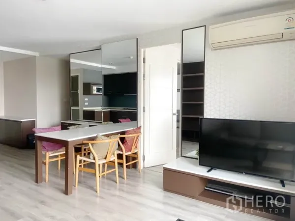 Condominium for rent in Watthana, Bangkok - Dining table beside mirrored wall facing a TV console with access to the kitchen area.