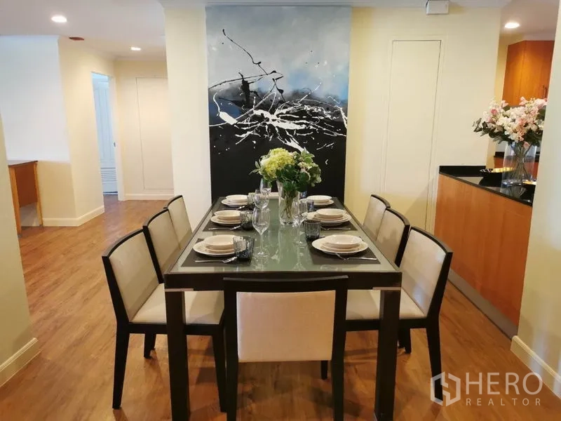 Condominium for rent in Watthana, Bangkok - Dining area set for six with glass-top table and large abstract artwork.