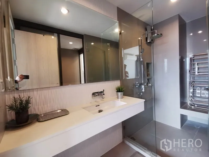 Condominium for rent in Khlong Toei, Bangkok - Modern bathroom with wide vanity, glass shower enclosure and rain shower.