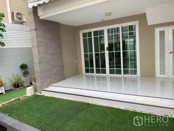 带办公室的家 出租或出售在Bang Na, Bangkok - 带顶前廊与白色推拉玻璃门，台阶与小草坪。