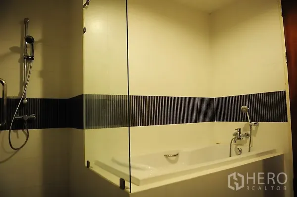 Condominium for rent in Pathum Wan, Bangkok - Modern bathroom with soaking bathtub, glass partition, handheld shower and striped tile accent.