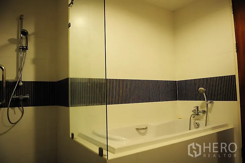 Condominium for rent in Pathum Wan, Bangkok - Modern bathroom with soaking bathtub, glass partition, handheld shower and striped tile accent.