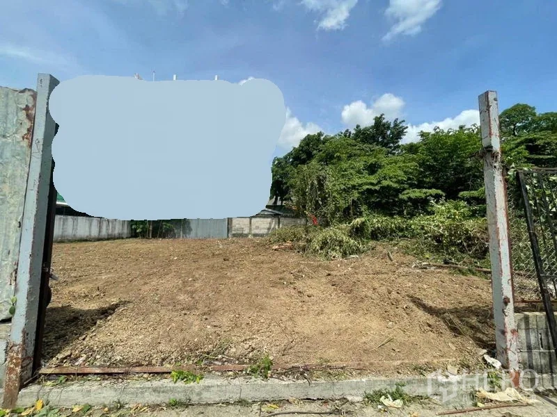 ที่ดิน ให้เช่าในMueang Nonthaburi, Nonthaburi - มุมมองจากหน้าประตูเหล็กเข้าสู่ที่ดินโล่ง ข้างแนวต้นไม้และรั้ว.