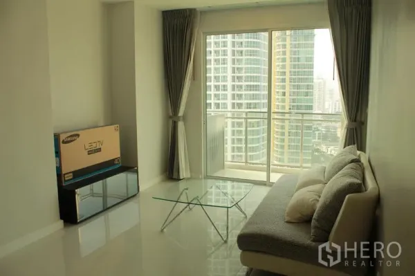Condominium for rent or sale in Watthana, Bangkok - Bright living room with sofa, glass coffee table, and a balcony overlooking the Bangkok skyline.