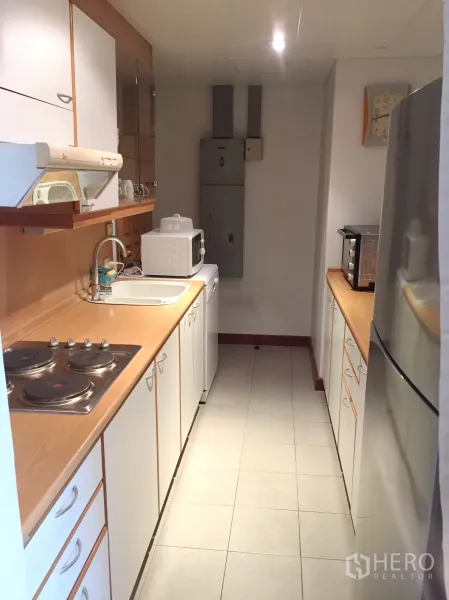 คอนโด ให้เช่าในPathum Wan, Bangkok - ครัวแบบทางเดิน ตู้สีขาว เคาน์เตอร์ไม้ เตาไฟฟ้า อ่างล้างจาน ไมโครเวฟ และตู้เย็นขนาดใหญ่