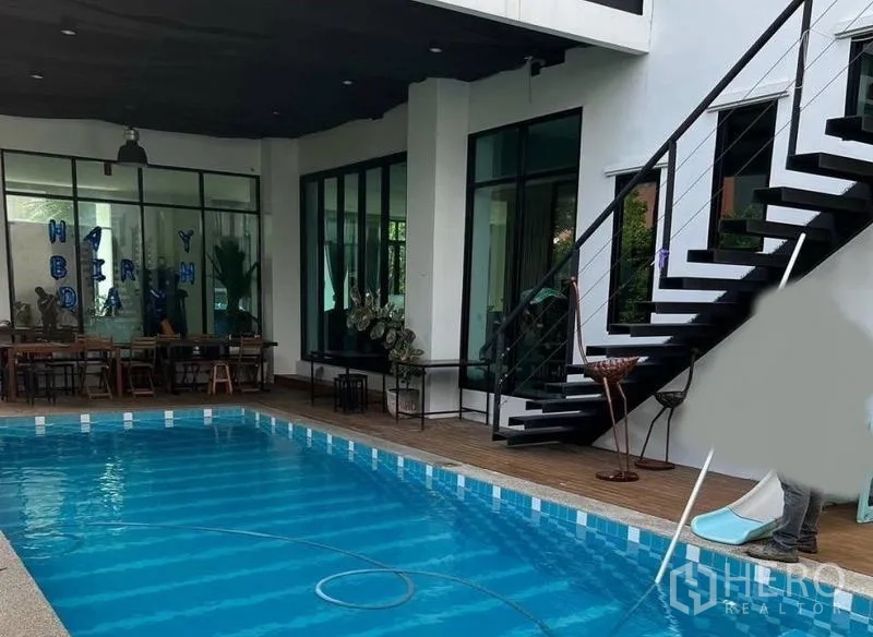 独立式住宅 出售在Pak Kret, Nonthaburi - 私家泳池配木平台、带顶露台与通往二层的金属楼梯。