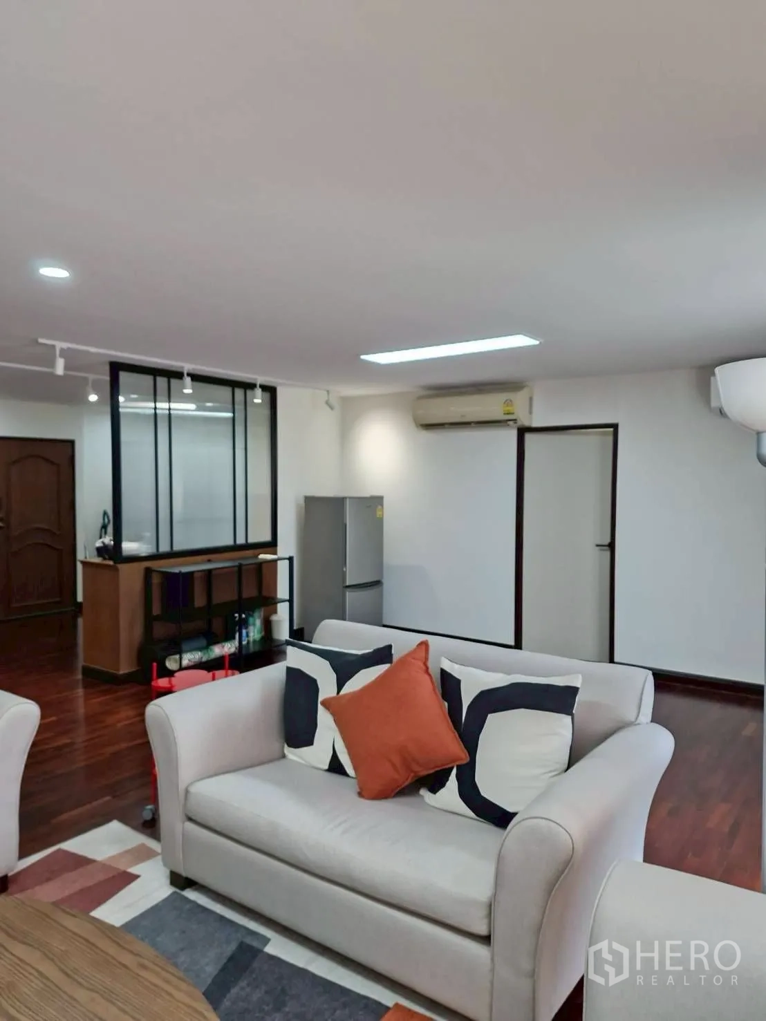 Condominium for rent in Khlong Toei, Bangkok - Open-plan living area with sofas, TV console, glass partition and wooden floors.