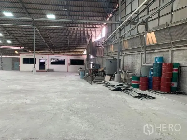Warehouse for rent - Long work bay with storage racks, barrels, and corrugated wall panels.
