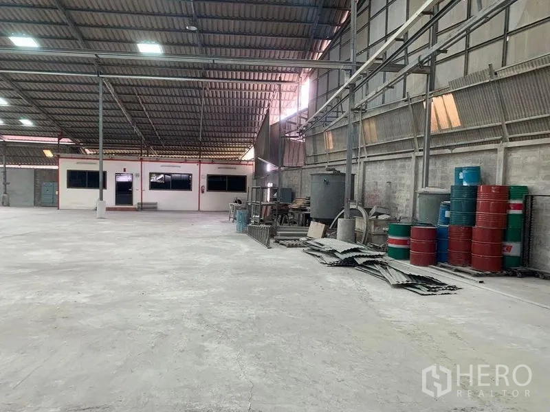 Warehouse for rent - Long work bay with storage racks, barrels, and corrugated wall panels.