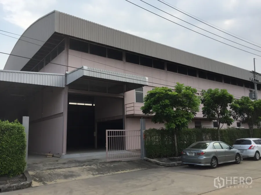 工厂 出租在Lam Luk Ka, Pathum Thani - 粉色外立面的工厂建筑，带卷帘门、入口大门与路边停车位