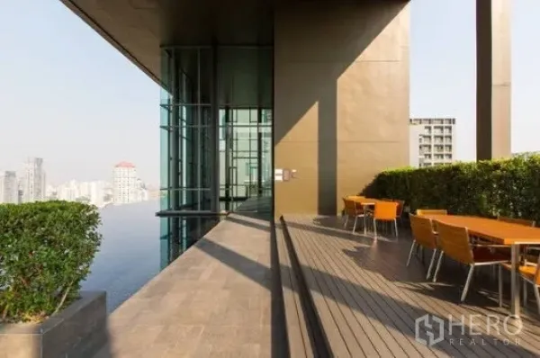 公寓 出租在Khlong Toei, Bangkok - 空中露台配桌椅，临近玻璃立面与绿篱，远眺城市景观。