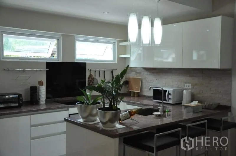 Townhouse for rent or sale in Watthana, Bangkok - Contemporary kitchen with island breakfast bar, pendant lights and glossy white cabinetry.