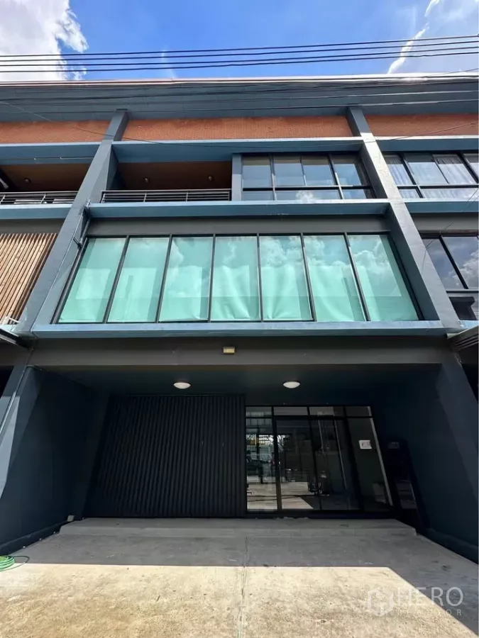 Townhouse for rent in Pak Kret, Nonthaburi - Modern three-storey townhouse facade with full-width glass and covered carport.