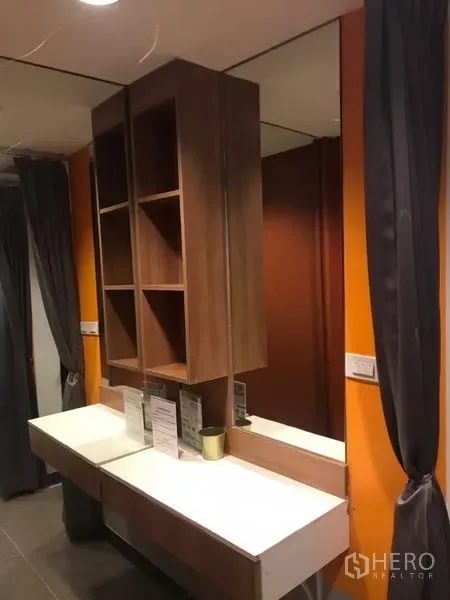Home Office for rent or sale in Khlong Toei, Bangkok - Built-in vanity with mirror and wooden shelving against an orange accent wall in a compact room.