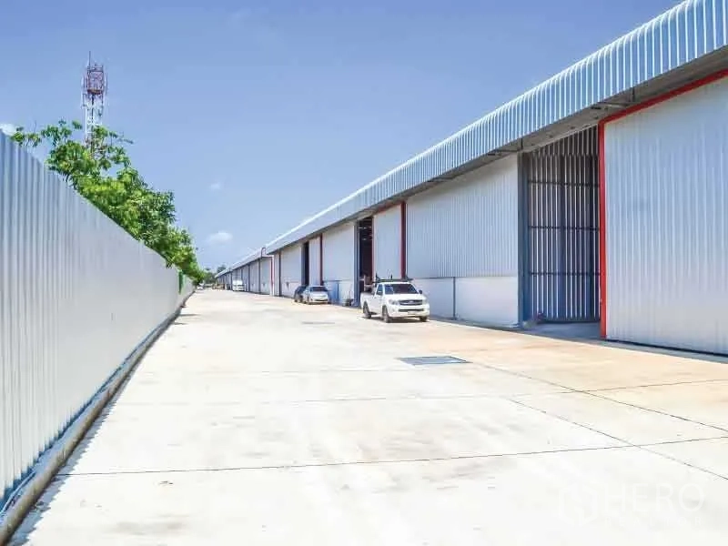 Warehouse for rent in Bang Phli, Samut Prakan - Modern warehouse exterior in Bang Phli, Samut Prakan with a wide concrete driveway and large roller shutter doors for truck access.
