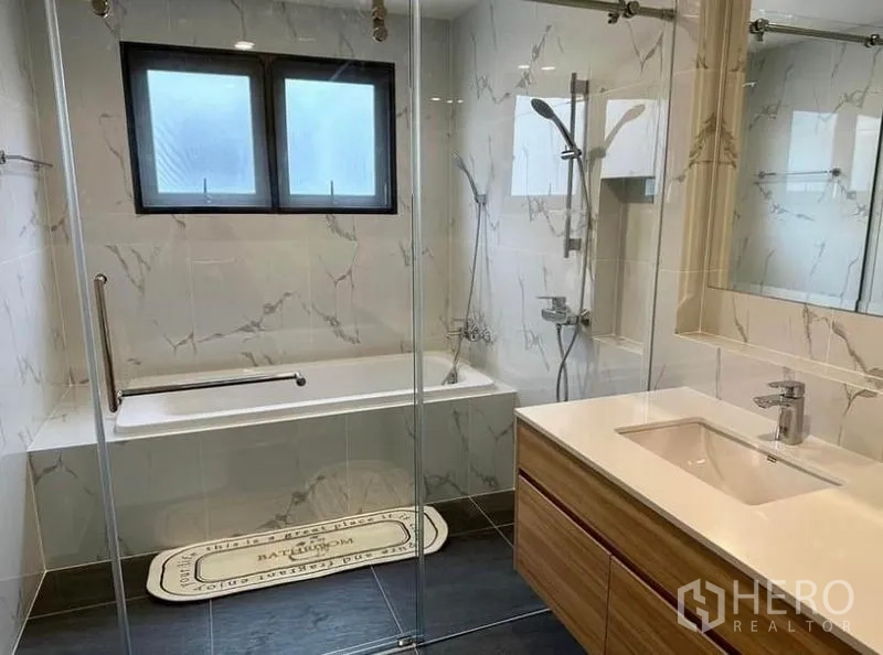 Detached House for rent in Bang Phli, Samut Prakan - Marble-tiled bathroom with bathtub, glass shower enclosure and a modern vanity.