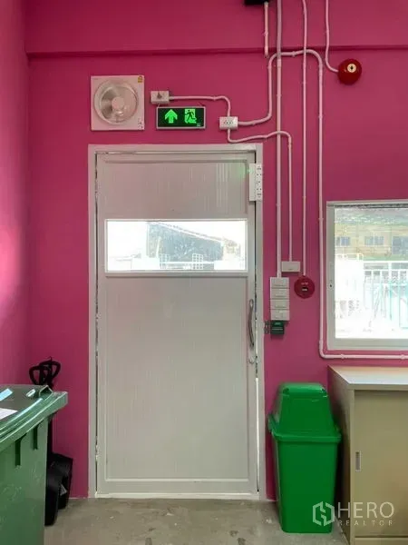 Warehouse for rent in Khlong Luang, Pathum Thani - Interior access door with ventilation fan, wiring and window beside a green bin.