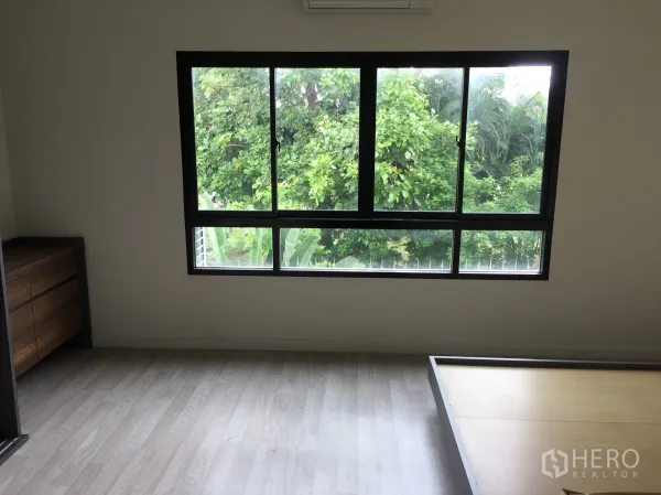 Townhouse for rent in Bang Kapi, Bangkok - Bedroom with large black-framed window overlooking lush greenery.