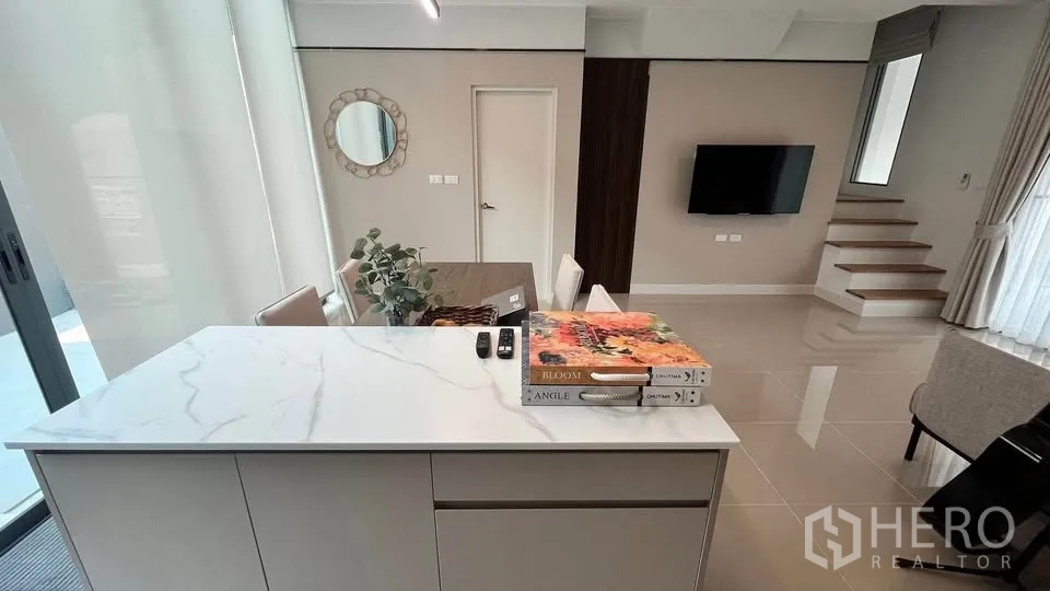 Townhouse for rent or sale in Bang Phli, Samut Prakan - Kitchen island facing TV wall and staircase beside large windows.