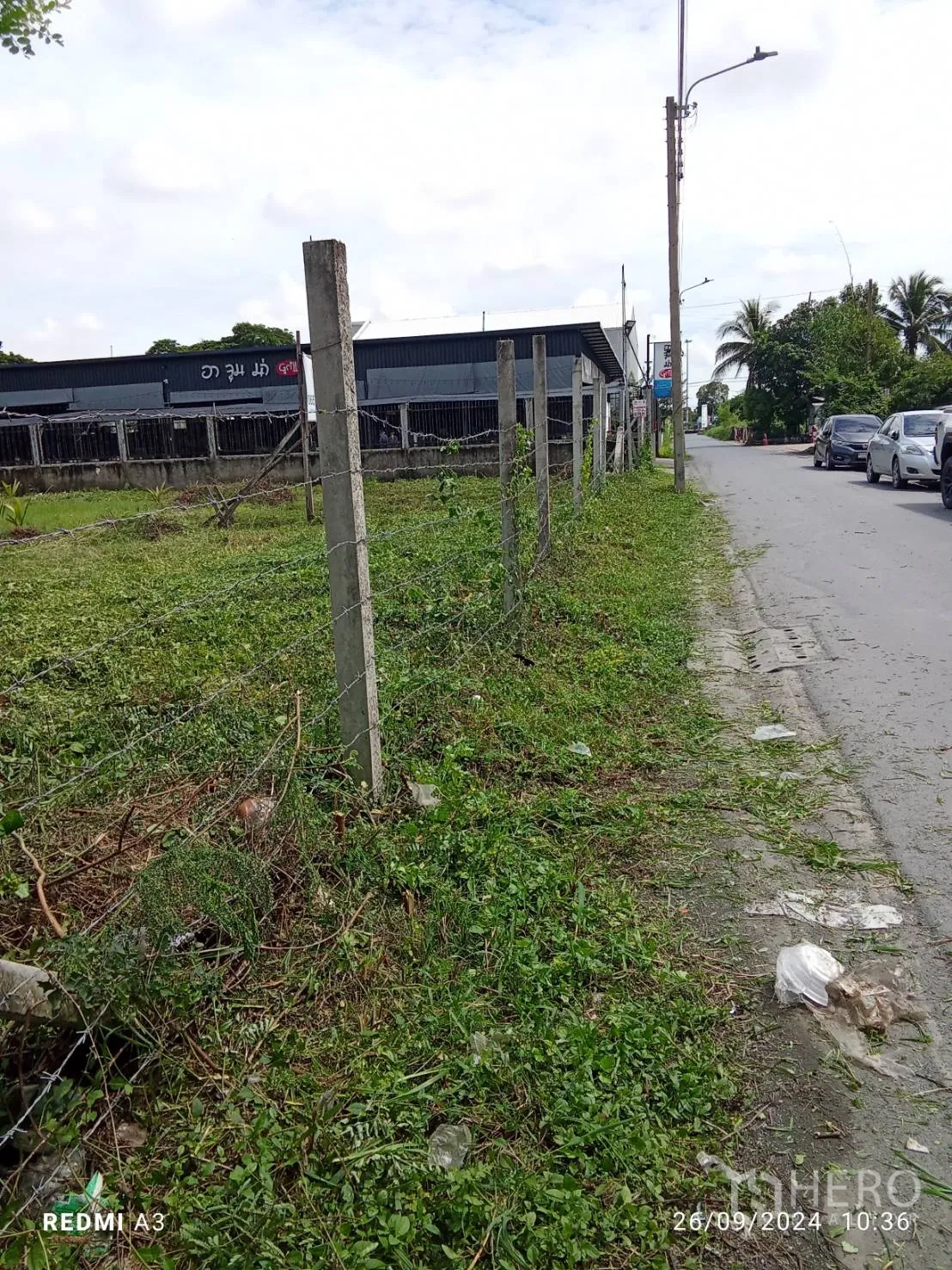 Land for rent in Khan Na Yao, Bangkok - Roadside view along the barbed‑wire fence bordering the land, with cars and streetlights visible.