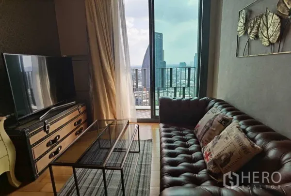 公寓 出租或出售在Khlong Toei, Bangkok - 客厅配皮质沙发、玻璃茶几与电视柜，落地窗连接阳台俯瞰城市。