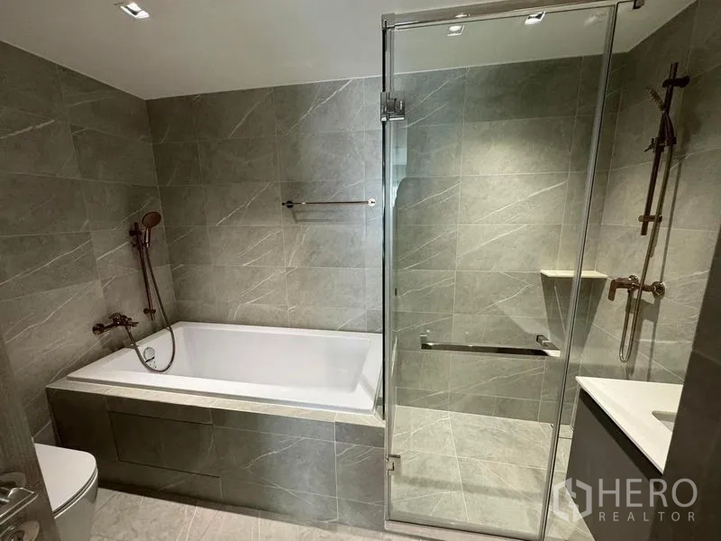 Condominium for rent in Watthana, Bangkok - Modern bathroom with a bathtub, separate glass shower and stone tile walls.