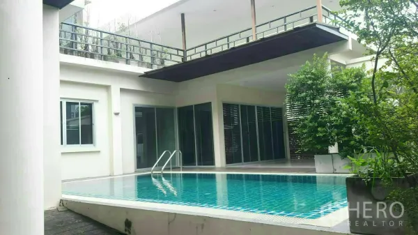 Detached House for rent or sale in Prawet, Bangkok - Courtyard view of a rectangular pool with ladder, upper terrace with glass railing and lush plants.