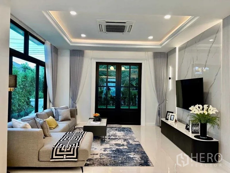 Detached House for rent in Bang Phli, Samut Prakan - Bright living room with marble TV wall, large windows and L-shaped sofa.